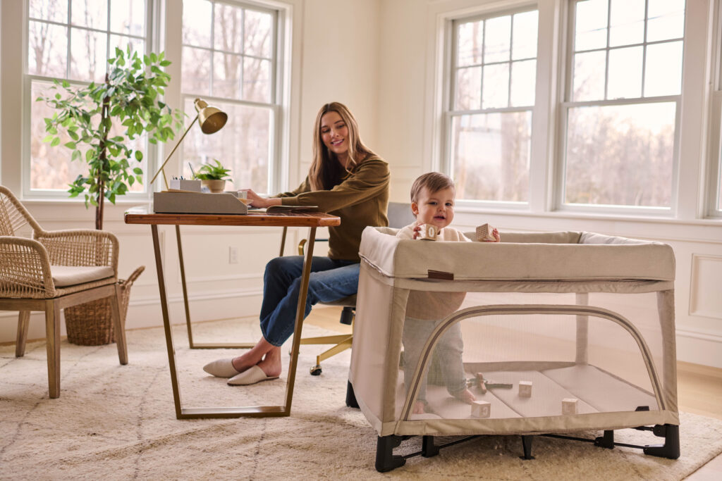 A caring mother looking at her little playing in the UPPAbaby Remi Playard.