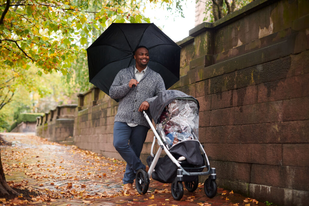 A father with his little one safely secured from rainy weather in their UPPAbaby Vista V2 with the Performance Rain Shield accessory