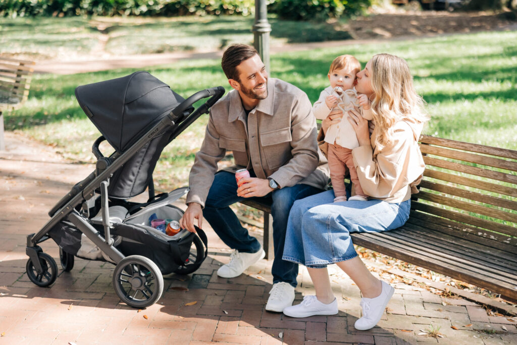 Parents sitting on a park bench with their child next to an UPPAbaby Cruz V2 stroller