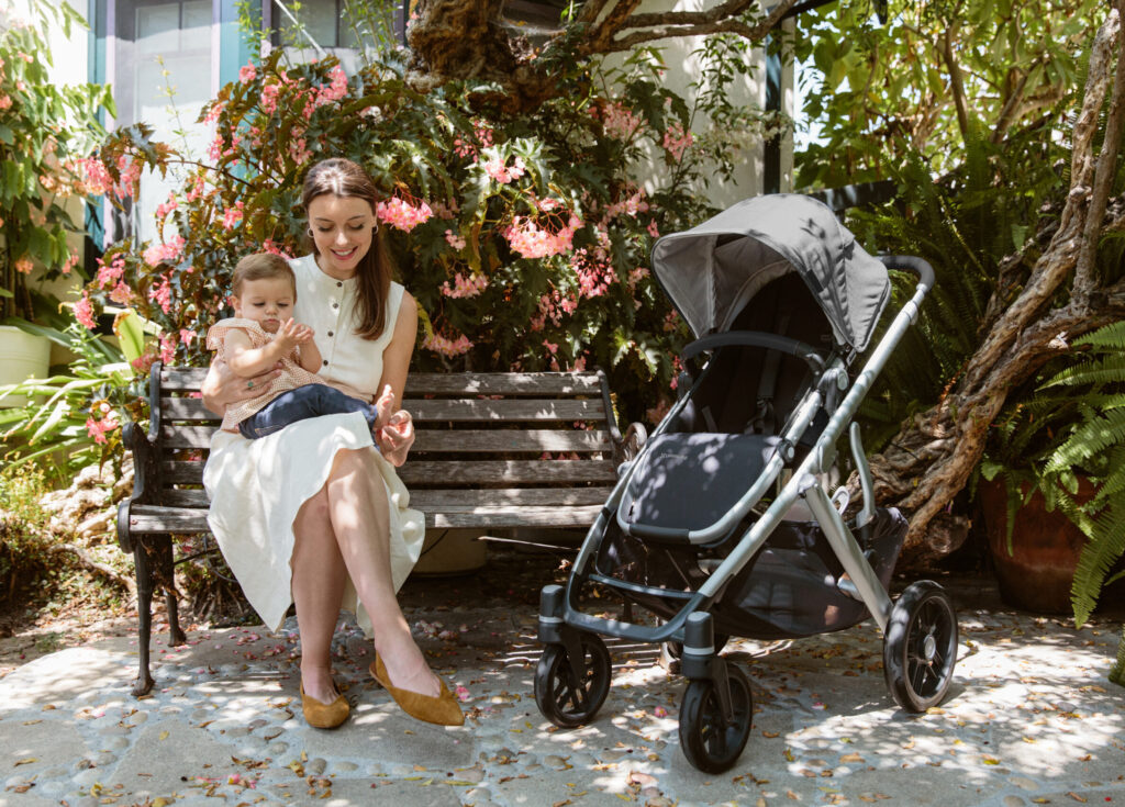 A mom and child sit on a bench beside their Vista V2 stroller with its wheels locked in place